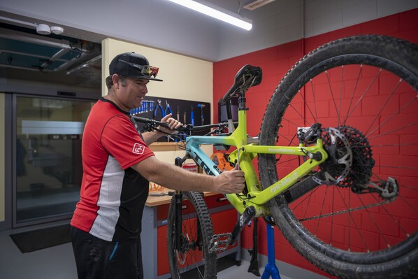 Una persona armando una bicicleta de montaña en una habitación con paredes rojas y una ventana.