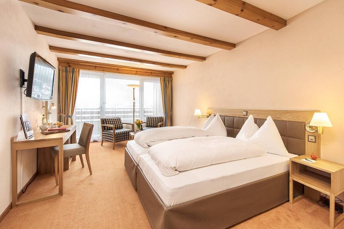 A hotel room with a large bed, a desk with a chair, a television, and a window with curtains.