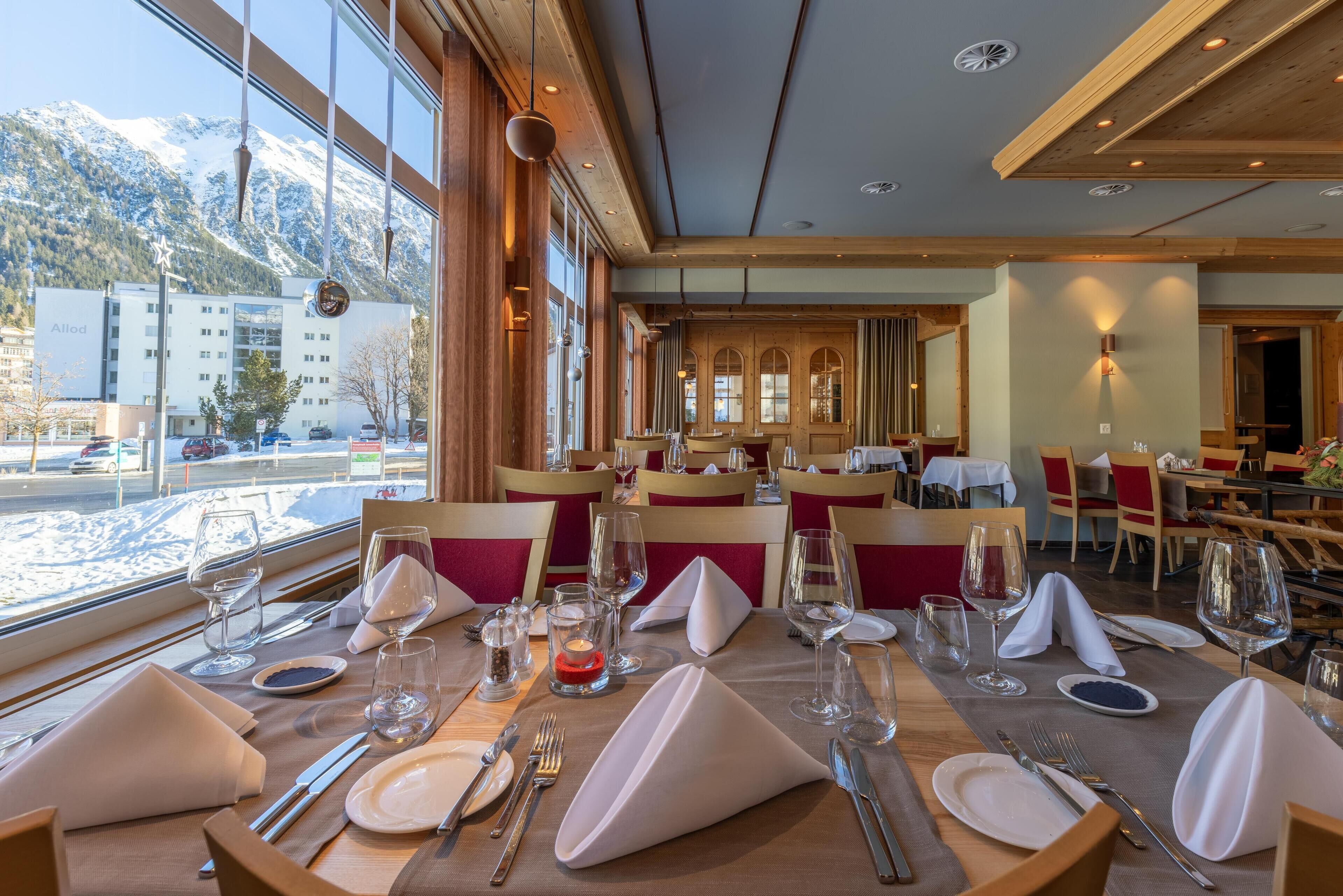 A restaurant with tables set for dining, large windows with a mountain view, and wooden interior design.