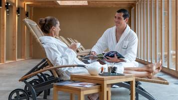 Une salle de spa avec des poutres en bois, une table de massage, un fauteuil pour massage des pieds et une table avec une théière et des tasses.
