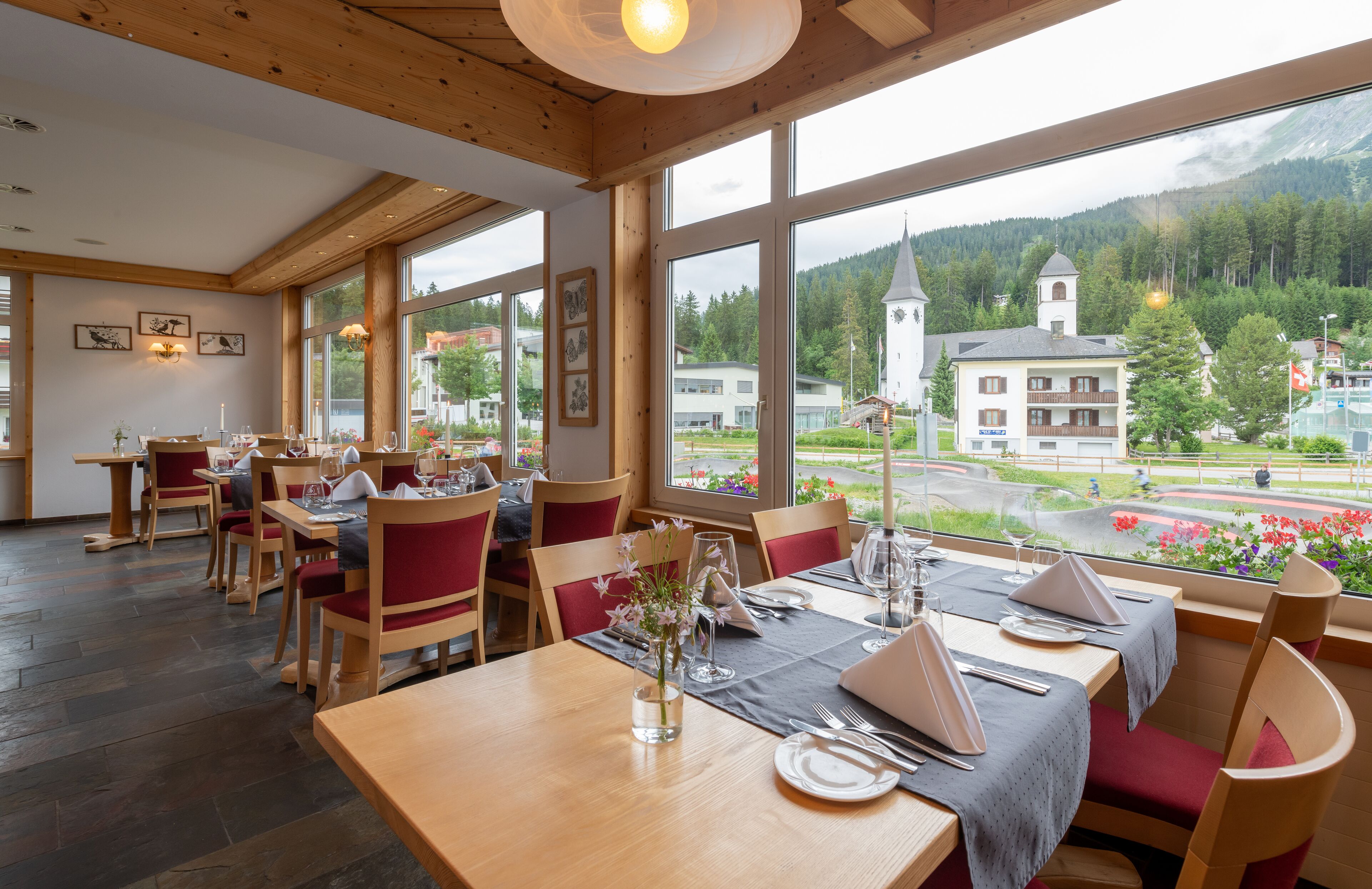Een restaurant met houten inrichting, grote ramen en uitzicht op een stad en bergen.