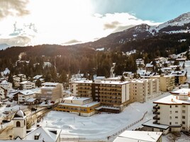 Un pueblo cubierto de nieve con varios edificios, incluyendo un hotel de varios pisos destacado, con balcones y un patio central.