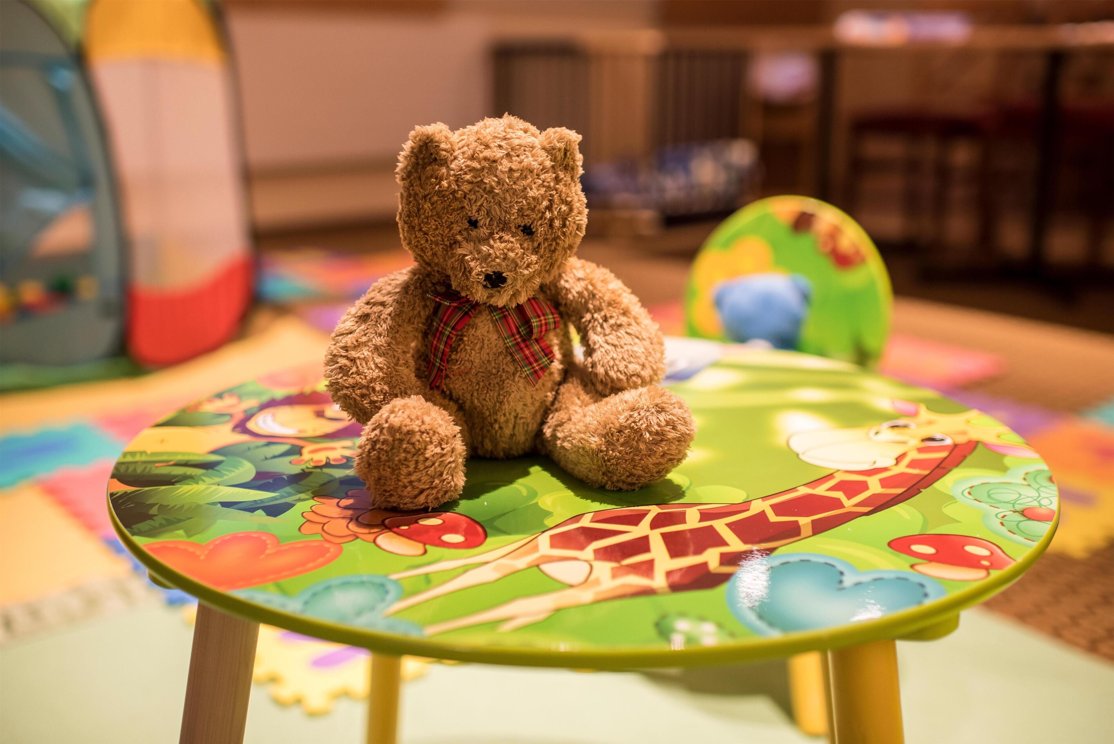 A brown teddy bear sitting on a colorful table with a giraffe design.