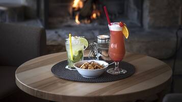 Una mesa redonda de madera con un bol de frutos secos, dos bebidas y una vela.