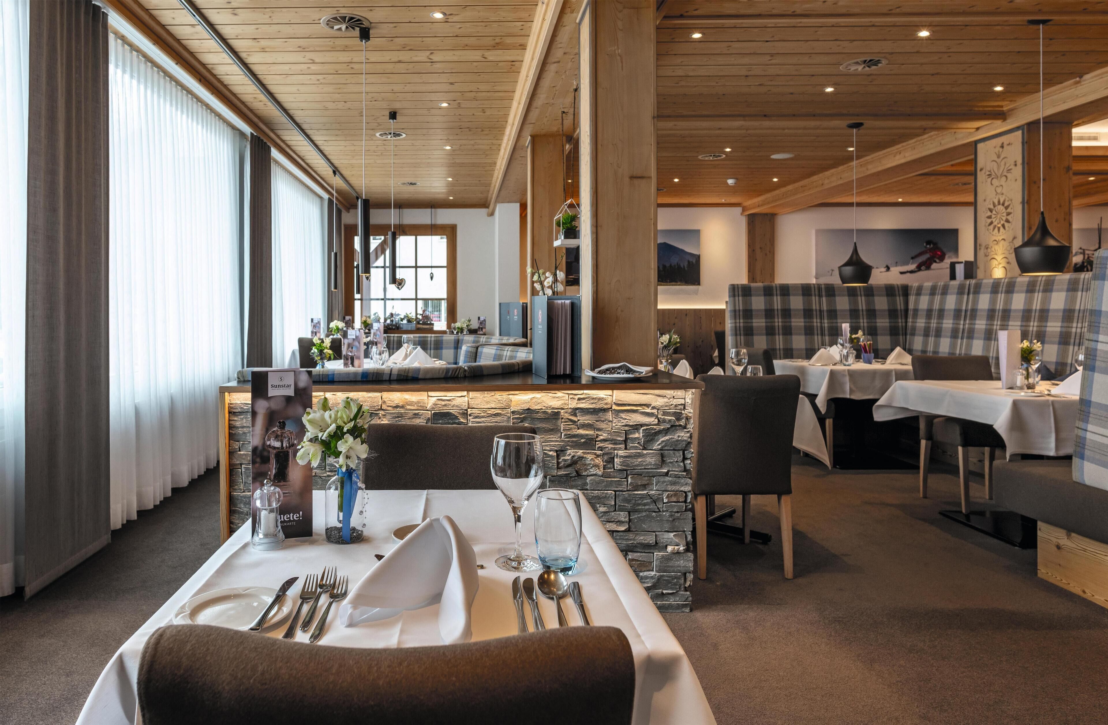 A restaurant with a stone wall, wooden ceiling, and a bar area. Tables are set with white tablecloths and silverware.