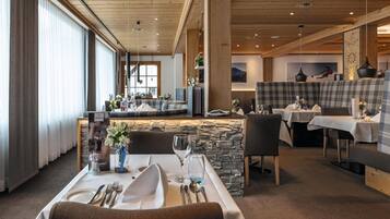 A restaurant with a stone wall, wooden ceiling, and a bar area. Tables are set with white tablecloths and silverware.