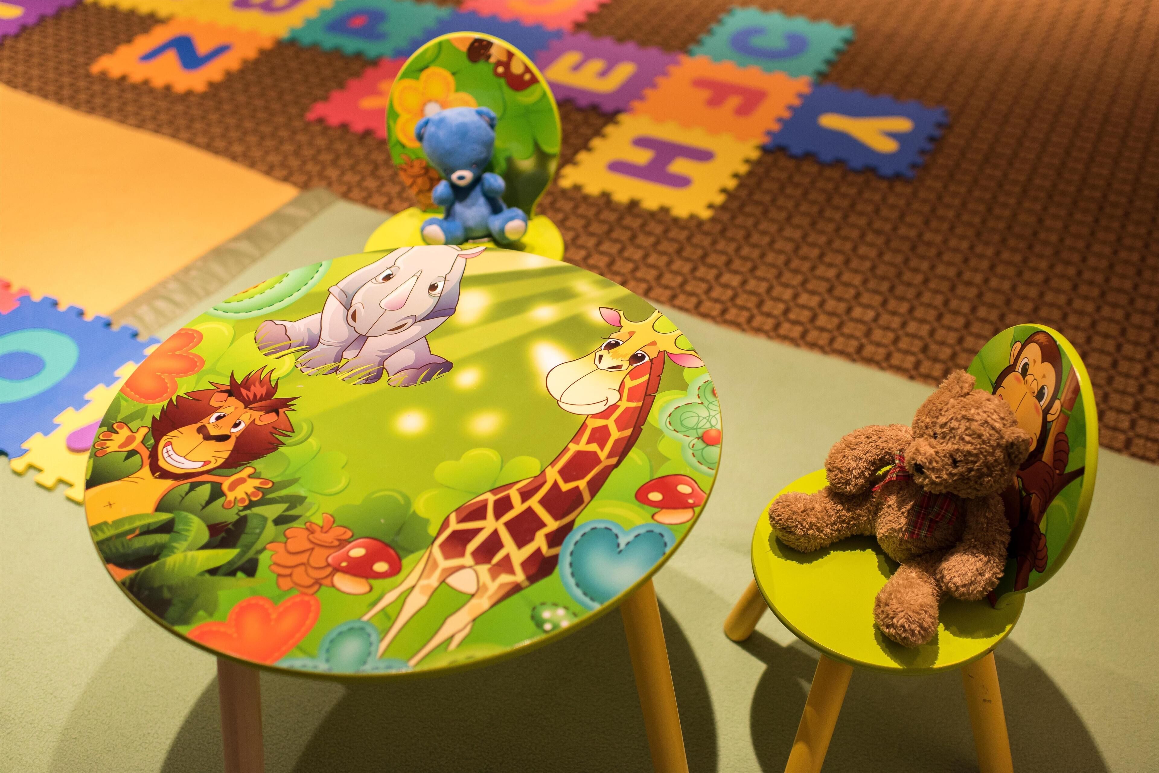 Un'area giochi per bambini con un tavolo e sedie colorati, con decorazioni a tema animali e personaggi.
