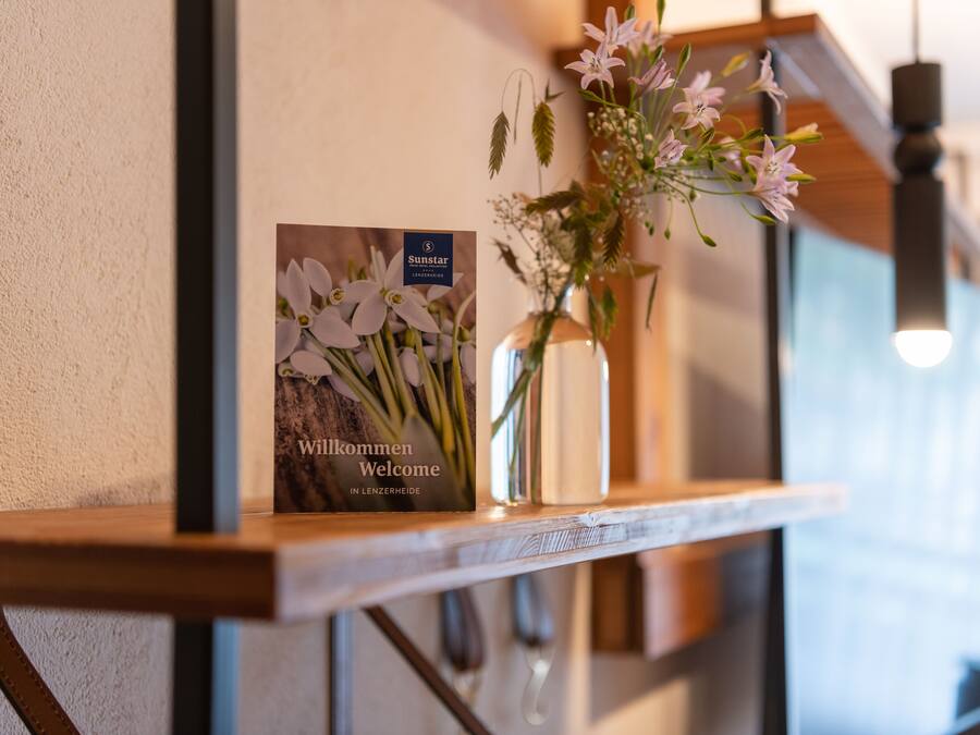 Schild mit Blumen und einer Vase auf einer Holzablage.