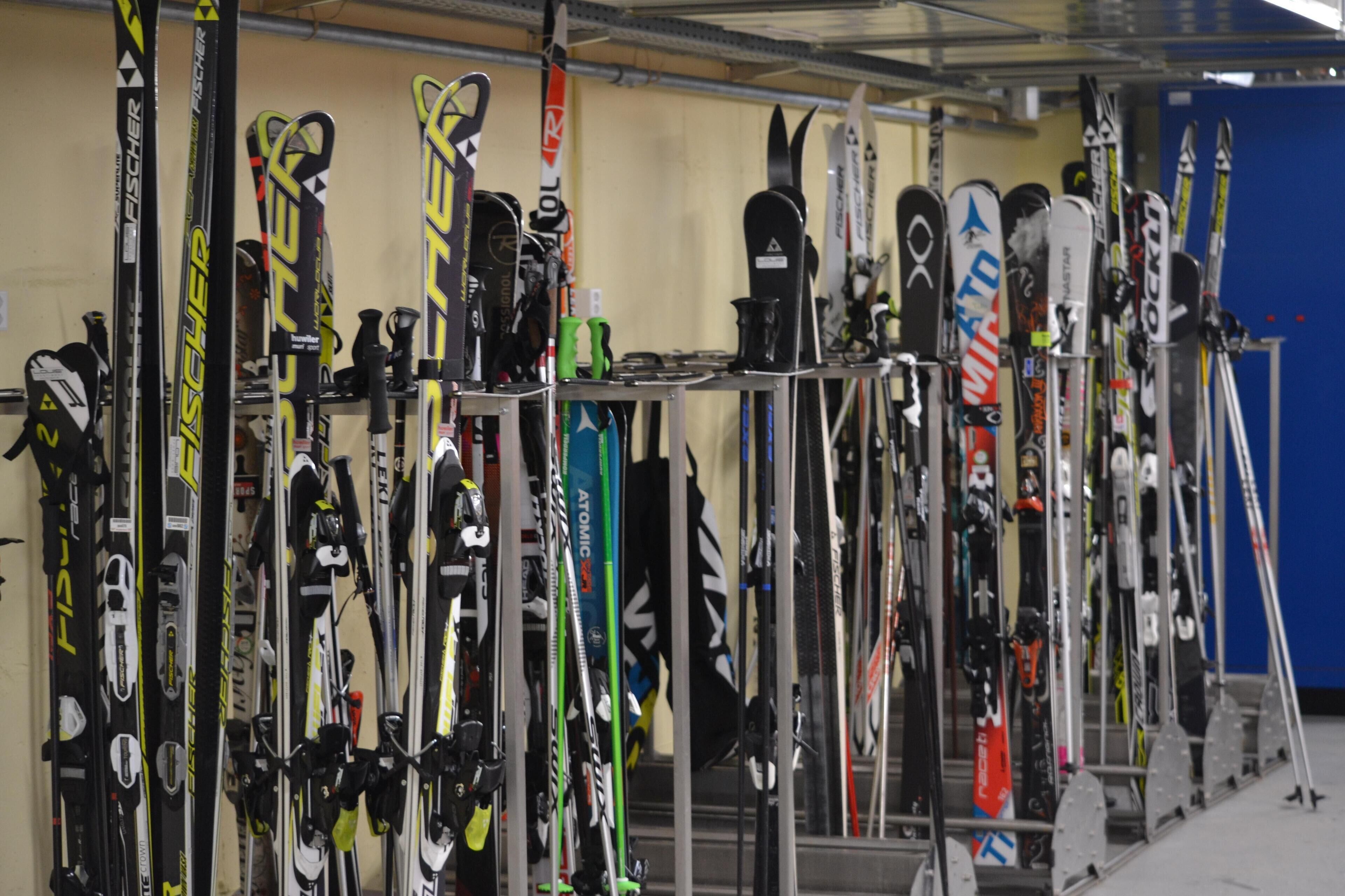 Une rangée de paires de skis et de snowboards, rangés sur des supports dans un espace de stockage.