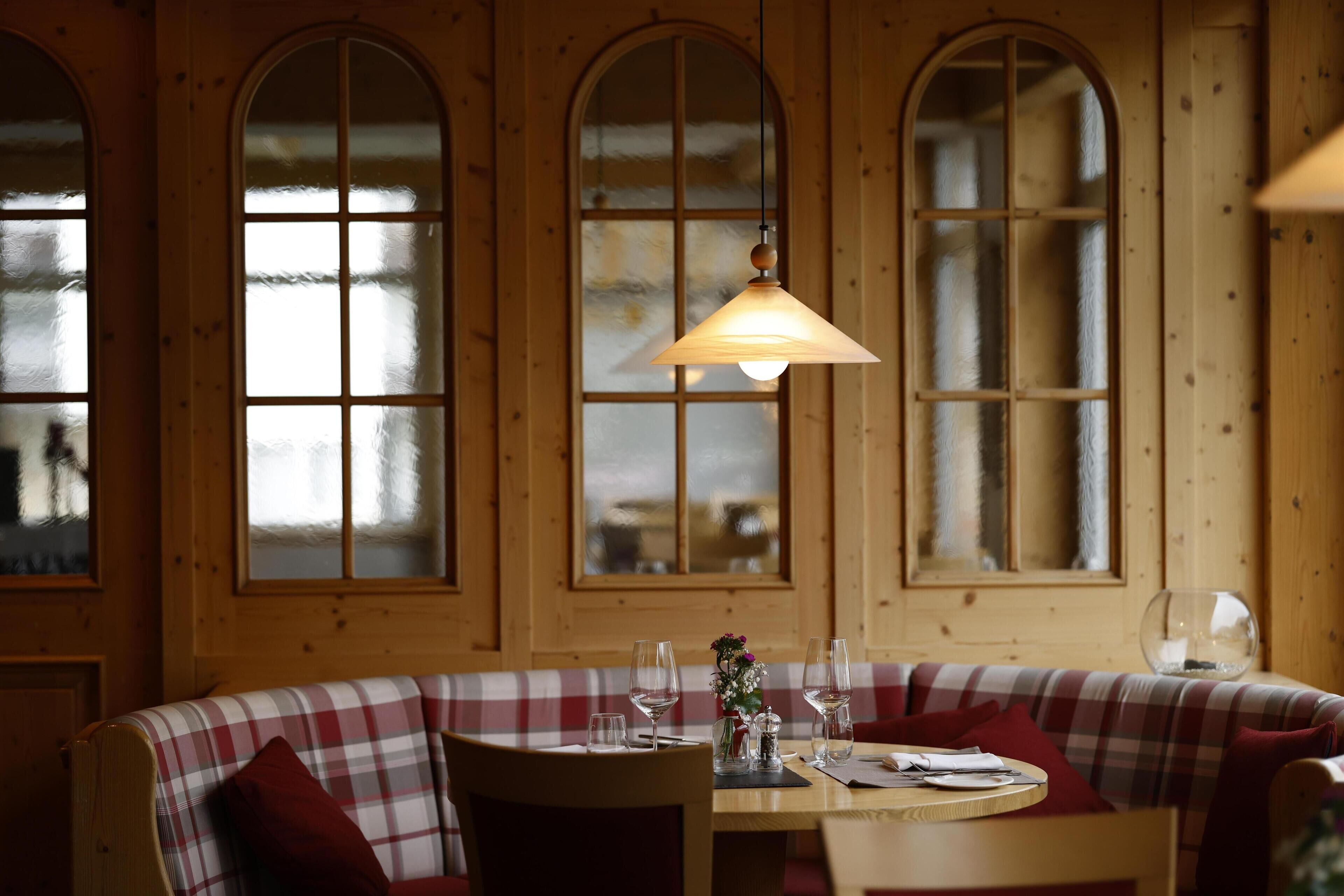 A cozy dining area with a wooden bench and table, large arched windows, and a hanging light fixture.