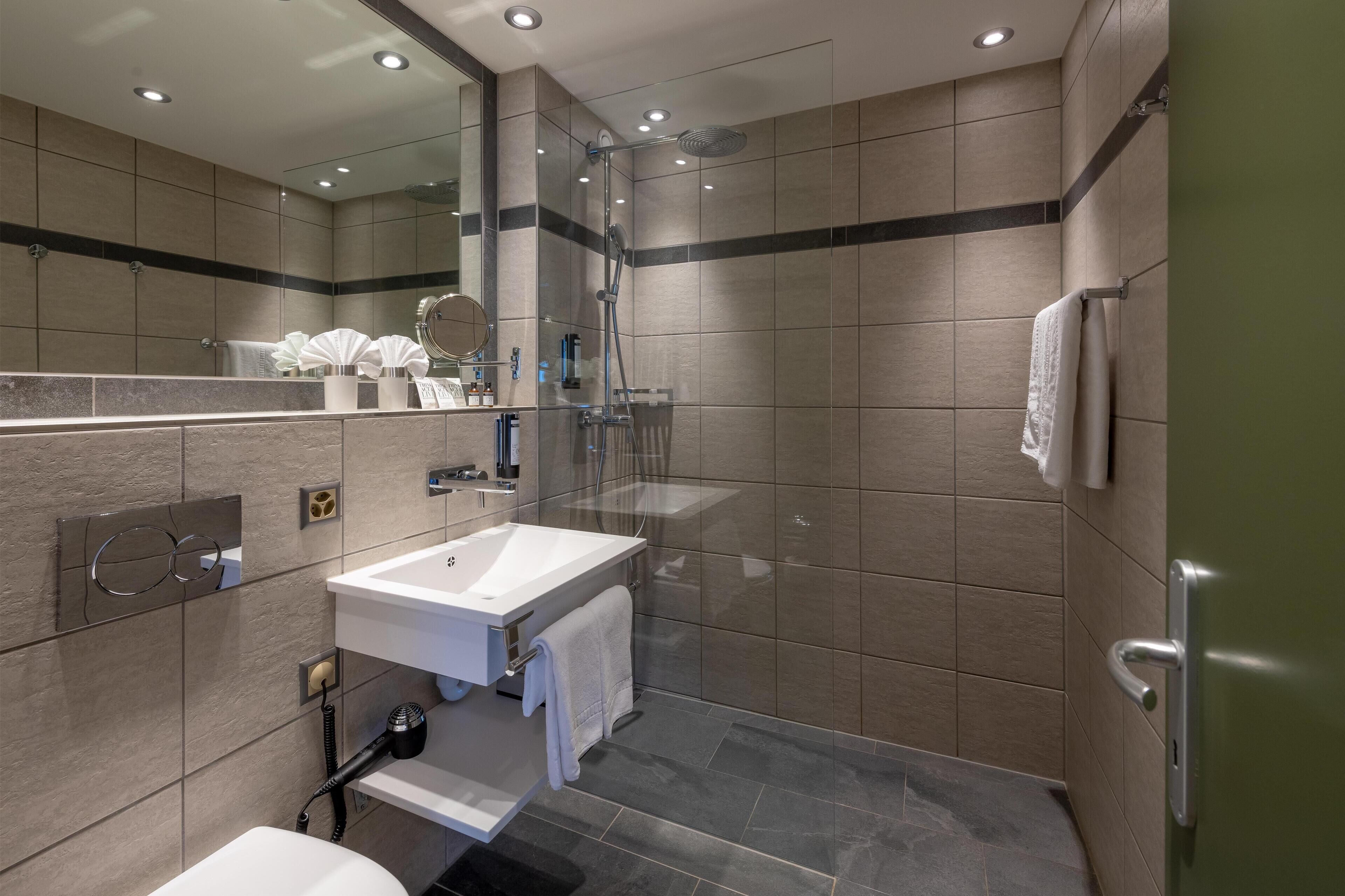 A modern bathroom with a glass-enclosed shower, a white sink, and a large mirror.