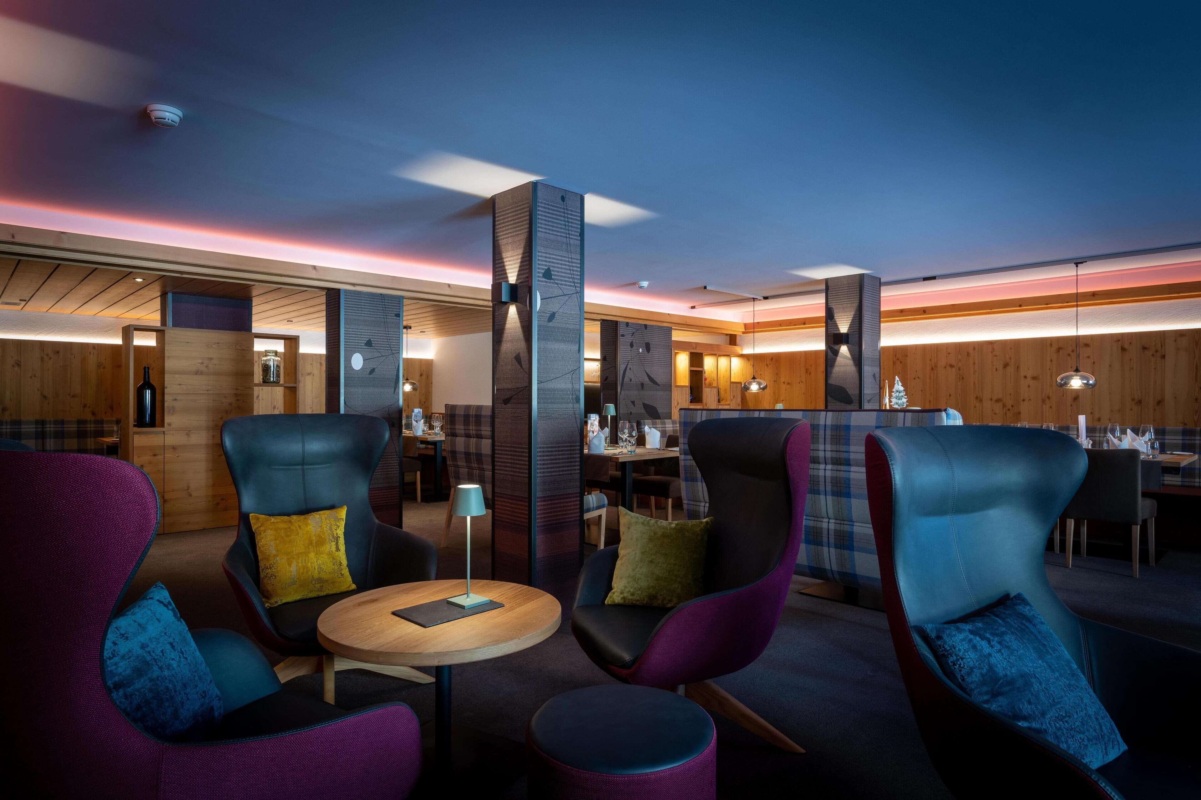 Un espace lounge moderne doté de sièges confortables, d’un bar en bois et d’un éclairage d’ambiance.