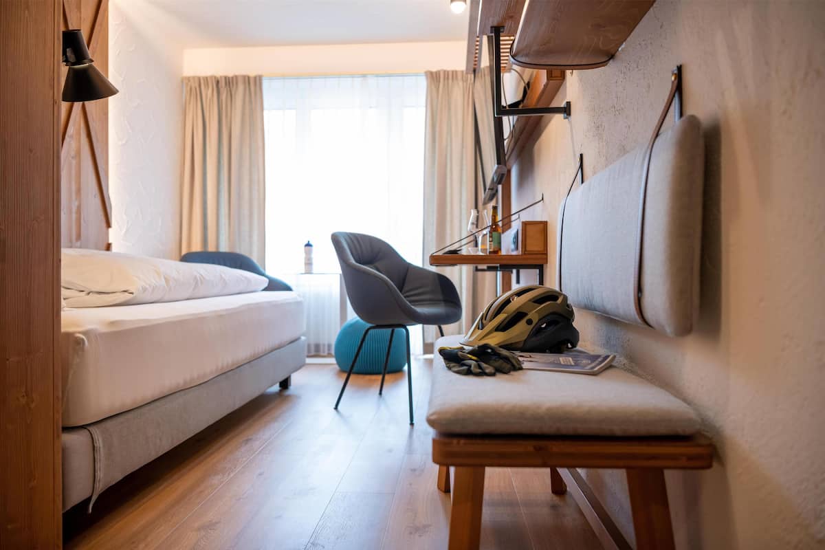 A hotel room with a bed, a chair, a small table, and a wall-mounted TV.