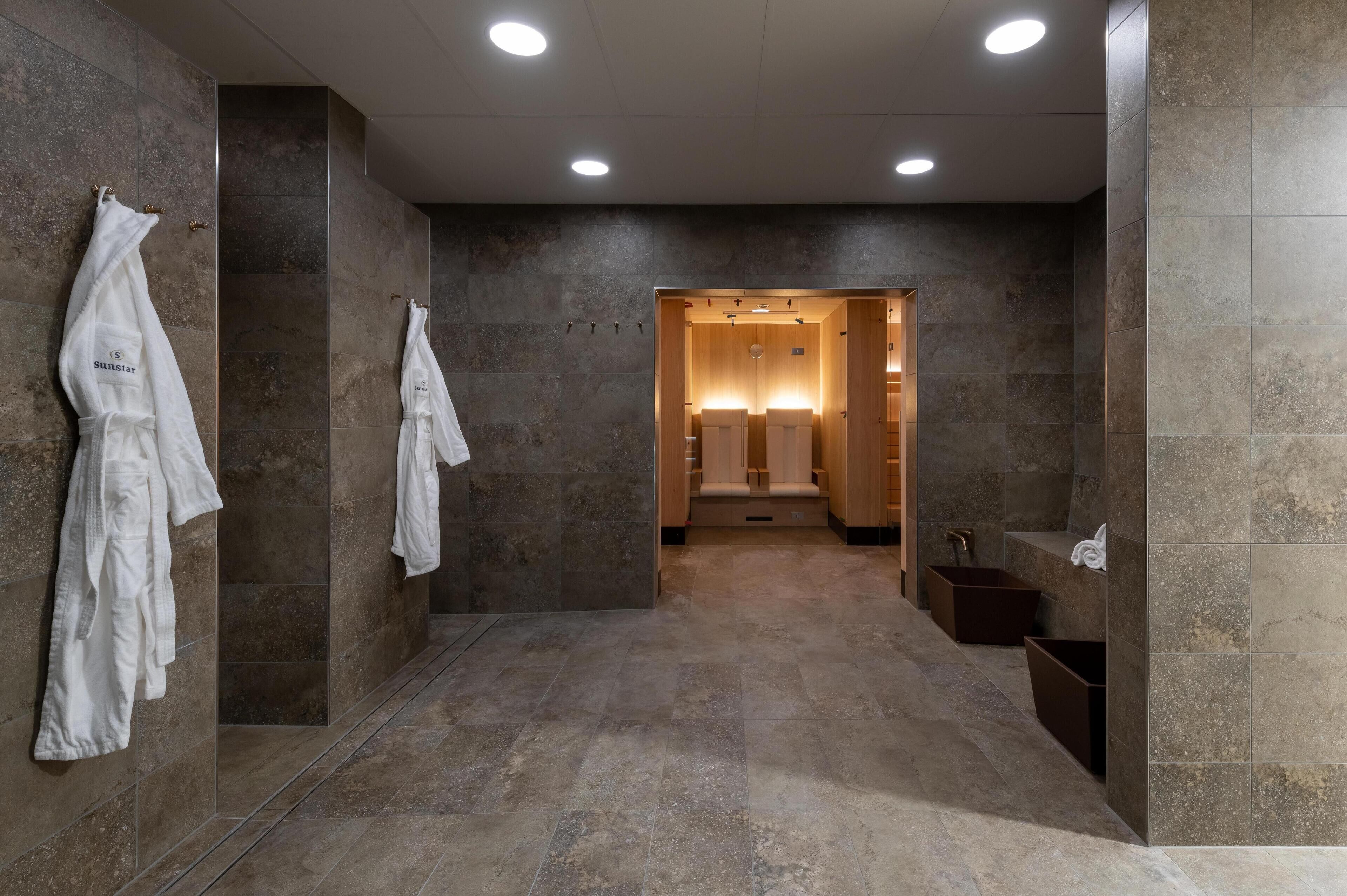 Ein modernes Badezimmer mit Marmorwänden und -boden, einer begehbaren Dusche sowie einem Schminktisch mit Spiegel und Waschbecken.
