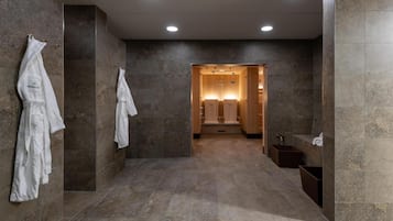 Ein modernes Badezimmer mit Marmorwänden und -boden, einer begehbaren Dusche sowie einem Schminktisch mit Spiegel und Waschbecken.