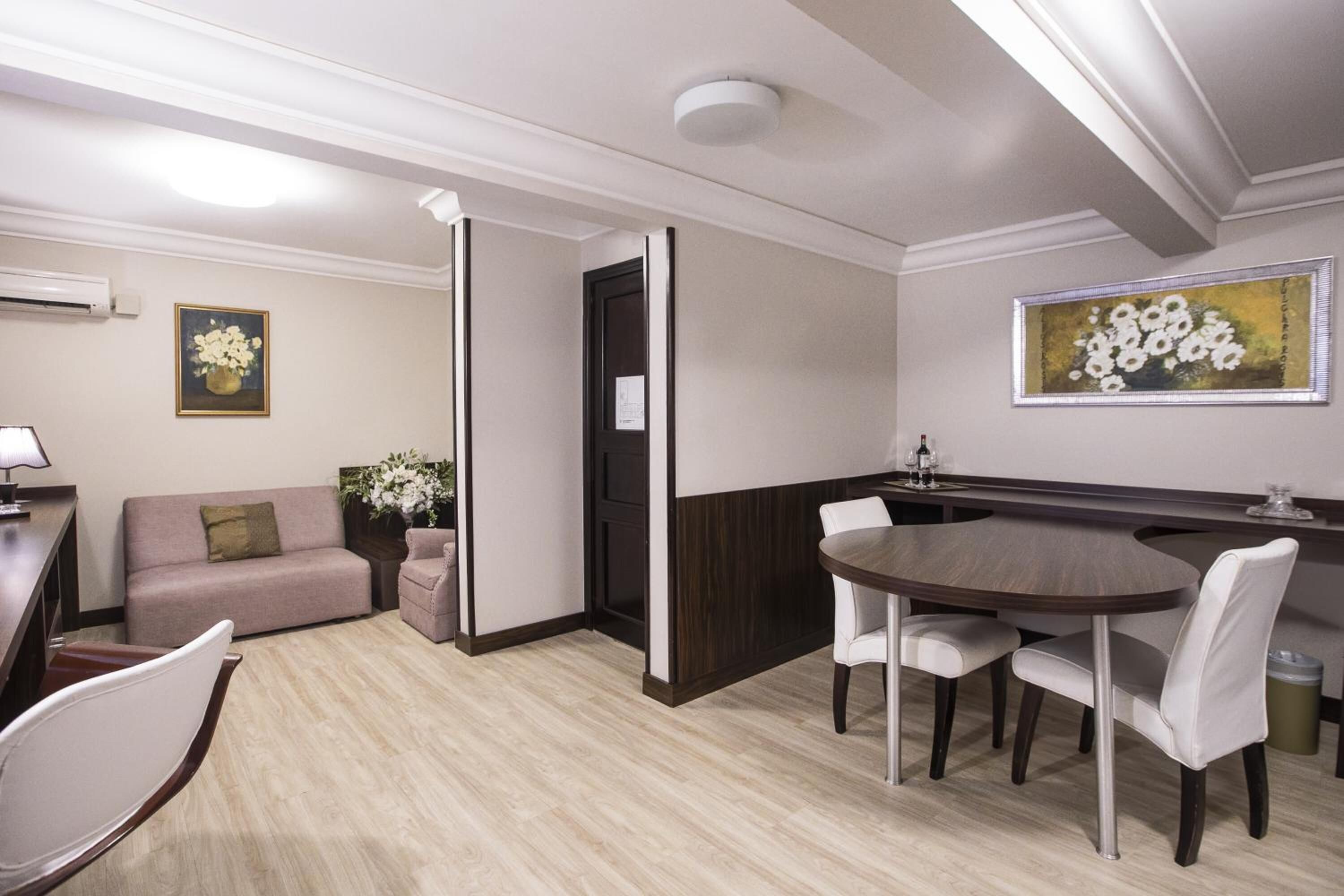 Habitación de hotel moderna con zona de comedor, sofá, mesita y un florero con flores.