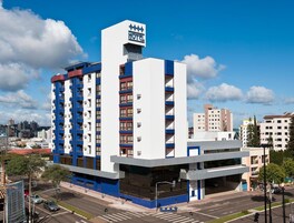 Un hotel de varios pisos con un llamativo letrero 'HOTEL' en la parte superior, fachada azul y blanca, y una estructura de estacionamiento en la parte inferior.