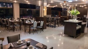 A modern restaurant with a clean, polished interior, featuring a central island with a vase of flowers, multiple dining tables, and a chandelier. - Hotel Lang Palace (Chapecó)