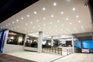 Un edificio moderno con fachada de vidrio, varios pisos y un amplio espacio de entrada con rampa y barandillas.