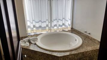 Un baño con bañera, una toalla y un ventanal con cortinas.