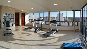 A gym with exercise equipment and large windows offering a city view. - Hotel Lang Palace (Chapecó)
