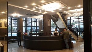 A hotel reception area with a curved desk, large windows, a staircase, and a chandelier. - Hotel Lang Palace (Chapecó)