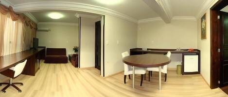 A room with a long wooden desk, a round table with chairs, a sofa, and a small cabinet.
