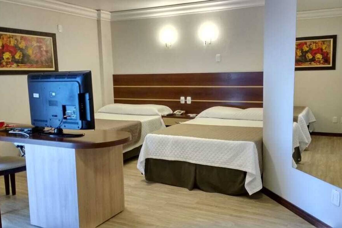 A hotel room with two beds, a desk with a computer, and a large mirror.
