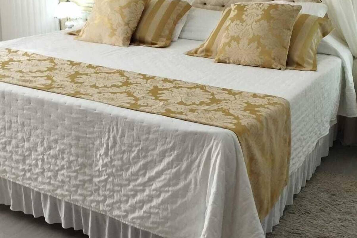 A bed with a tufted headboard, white bedding, and gold-patterned pillows.
