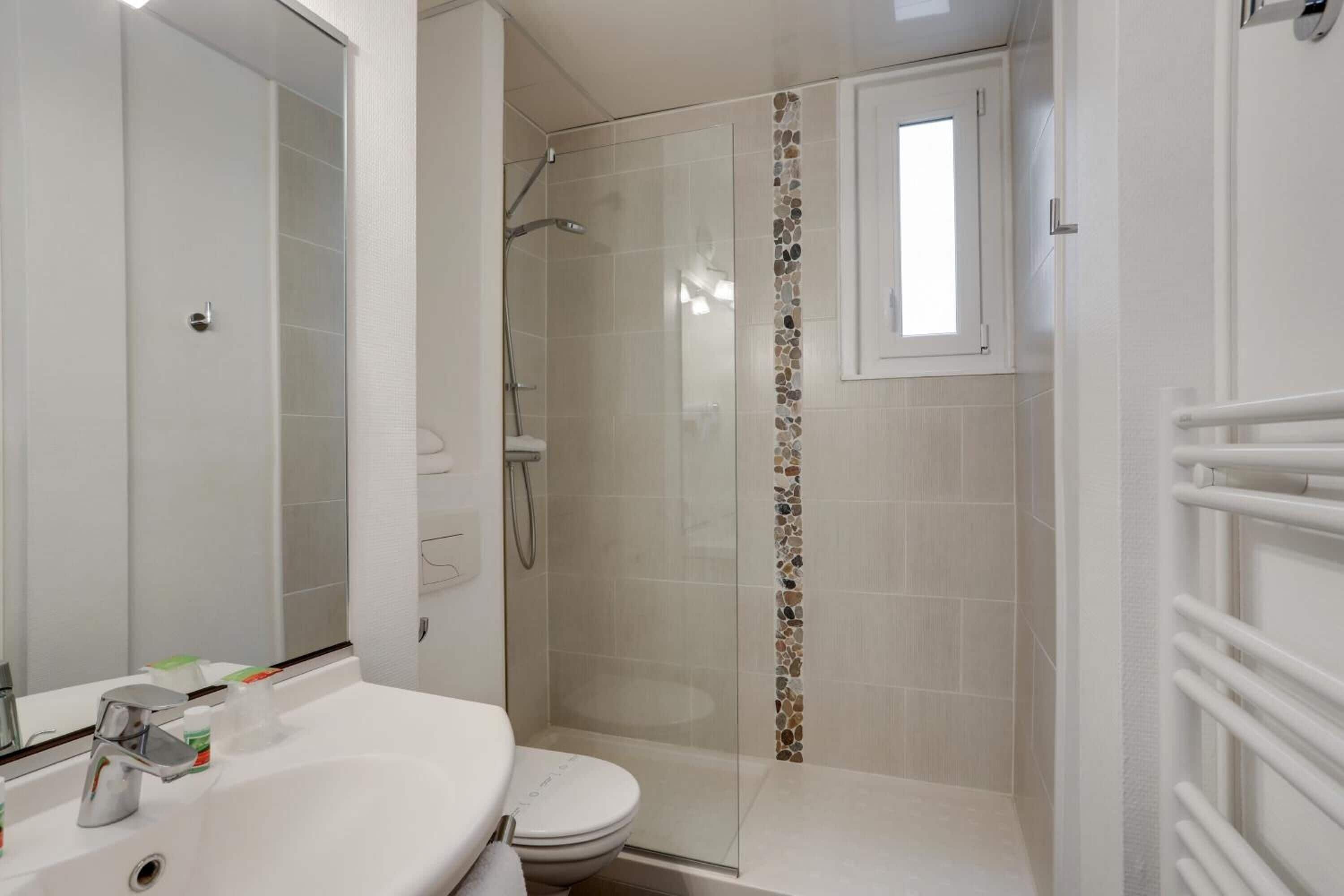 Un baño con lavamanos blanco, inodoro y zona de ducha con mampara de vidrio.