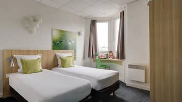 A hotel room with two beds, a desk, a chair, a radiator, and a window with curtains.