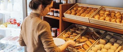 Vitrina de pastelería con diversos productos horneados y una persona alcanzando un pastel.