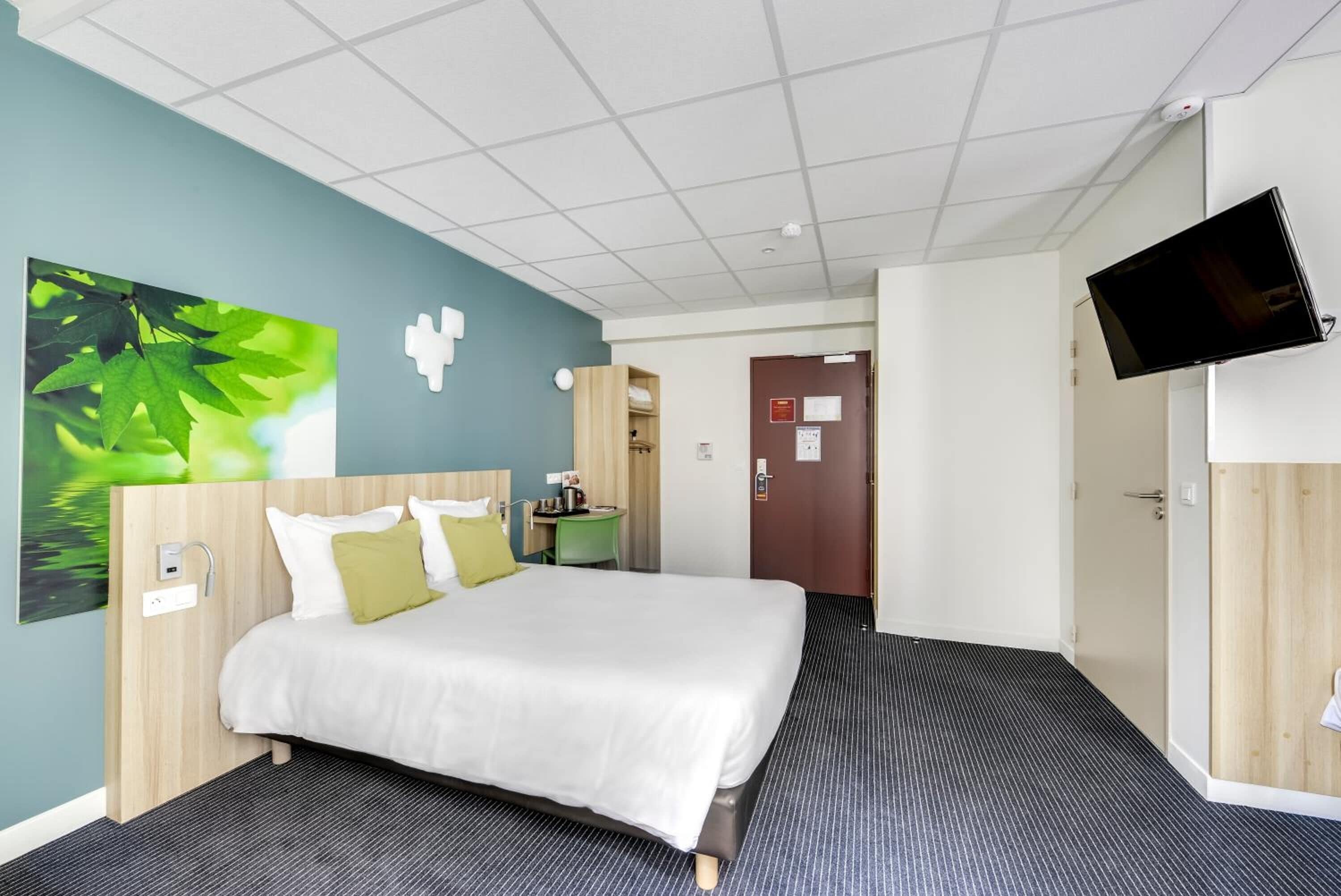 A hotel room with a bed, a desk, a chair, a TV, and a bathroom door.