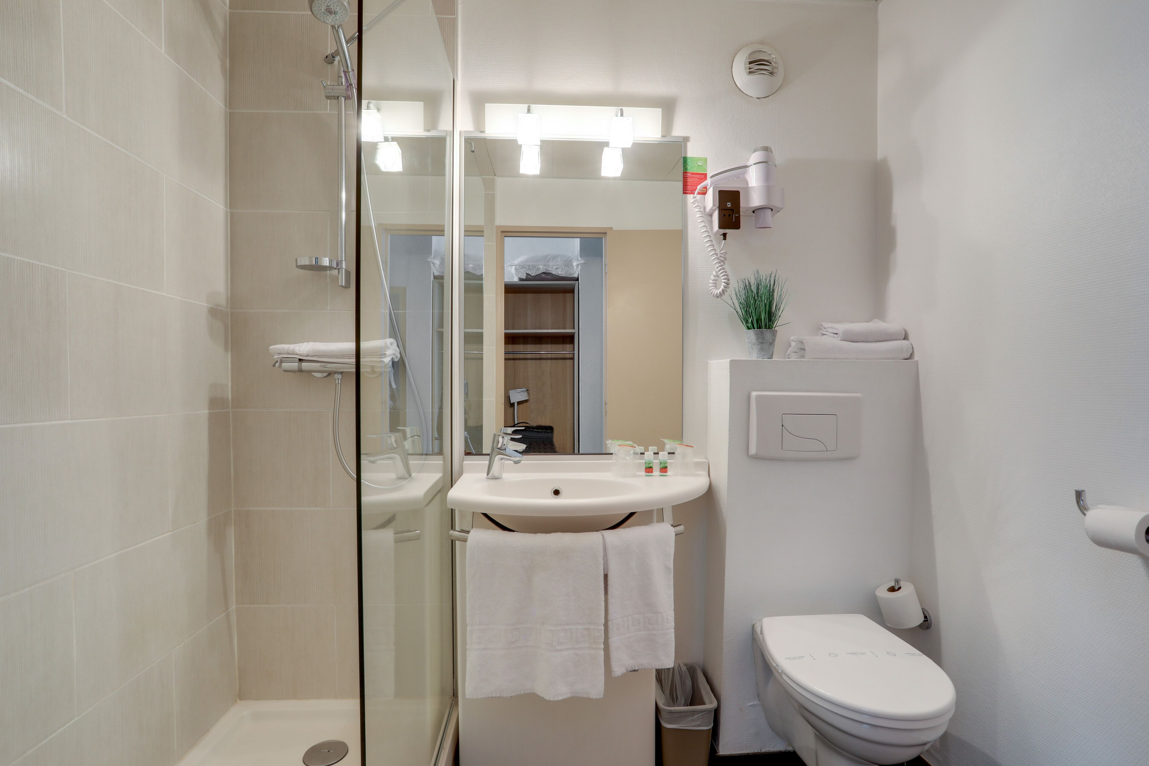 Een badkamer met een glazen douchecabine, een wastafel met spiegel, een toilet en een kleine prullenbak.