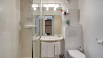 Une salle de bain avec une douche à parois de verre, un lavabo avec un miroir, des toilettes et une petite poubelle.