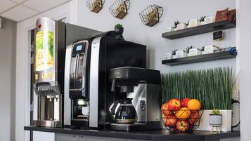 Una máquina de café y un dispensador de agua sobre una encimera con una cesta de frutas y una pequeña planta en maceta.