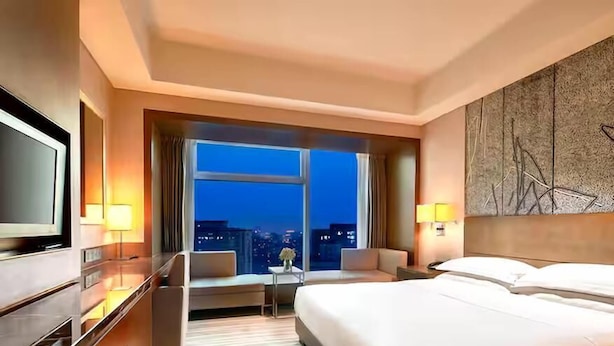 A hotel room with a large bed, a desk, a chair, a TV, and a city view.