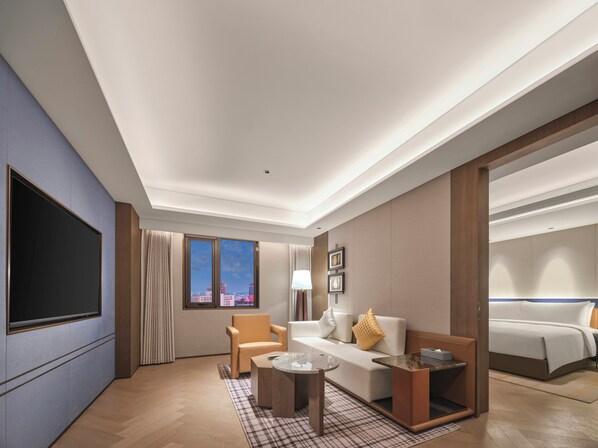 Une chambre d’hôtel équipée d’un grand téléviseur à écran plat, d’un canapé, d’un fauteuil, d’une petite table et d’un lit.