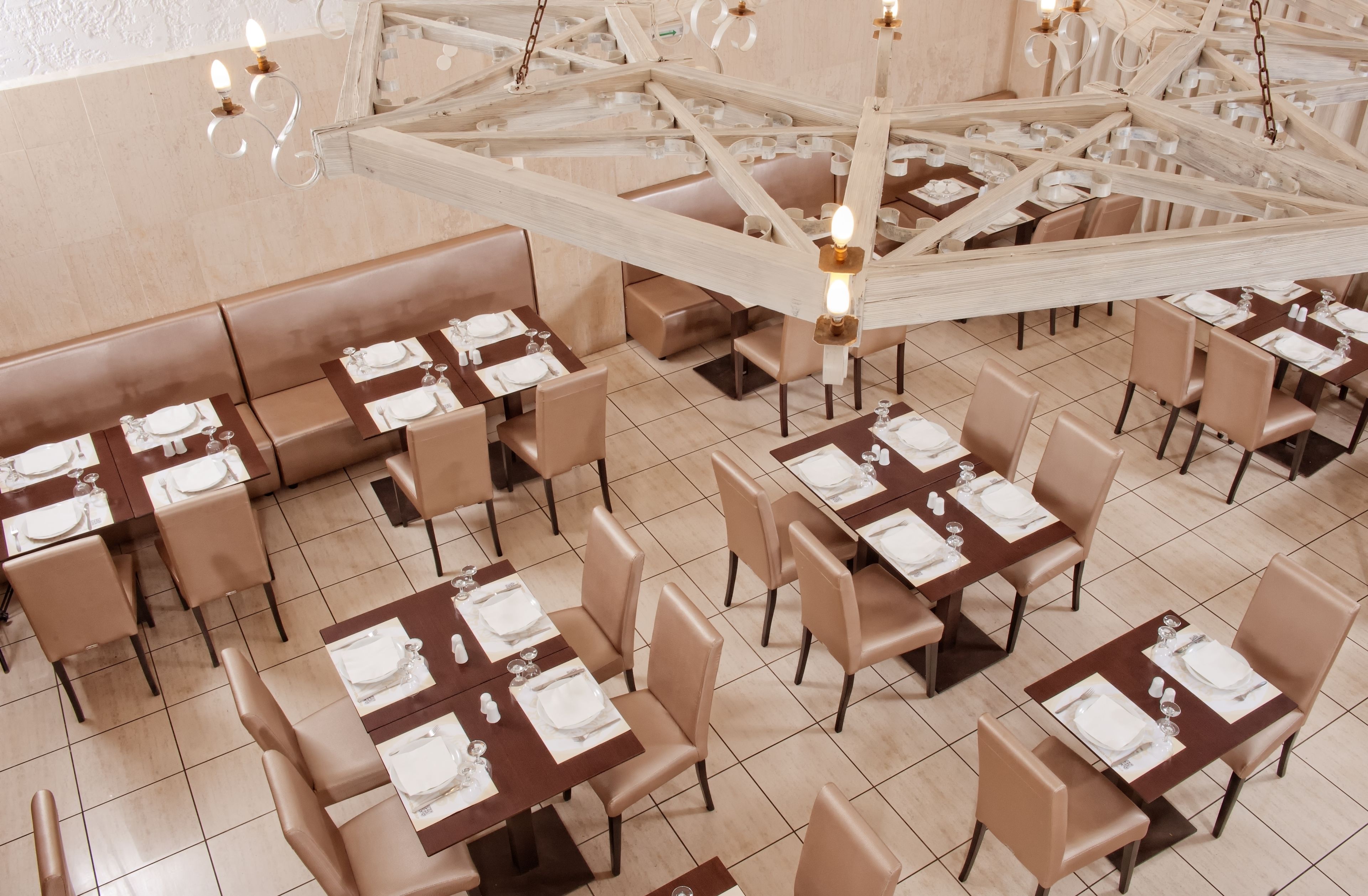 A restaurant with multiple tables set for dining, featuring a modern chandelier and beige seating.