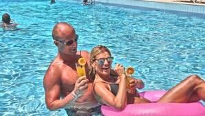 Una piscina con gente disfrutando del agua, algunos sosteniendo bebidas.