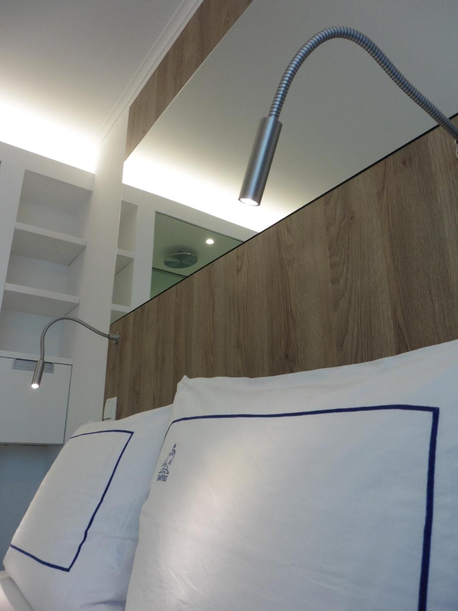 A modern hotel room with a wooden headboard, a white bed with blue trim, and a ceiling-mounted lamp.