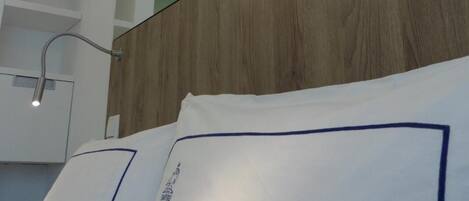 A modern hotel room with a wooden headboard, a white bed with blue trim, and a ceiling-mounted lamp.