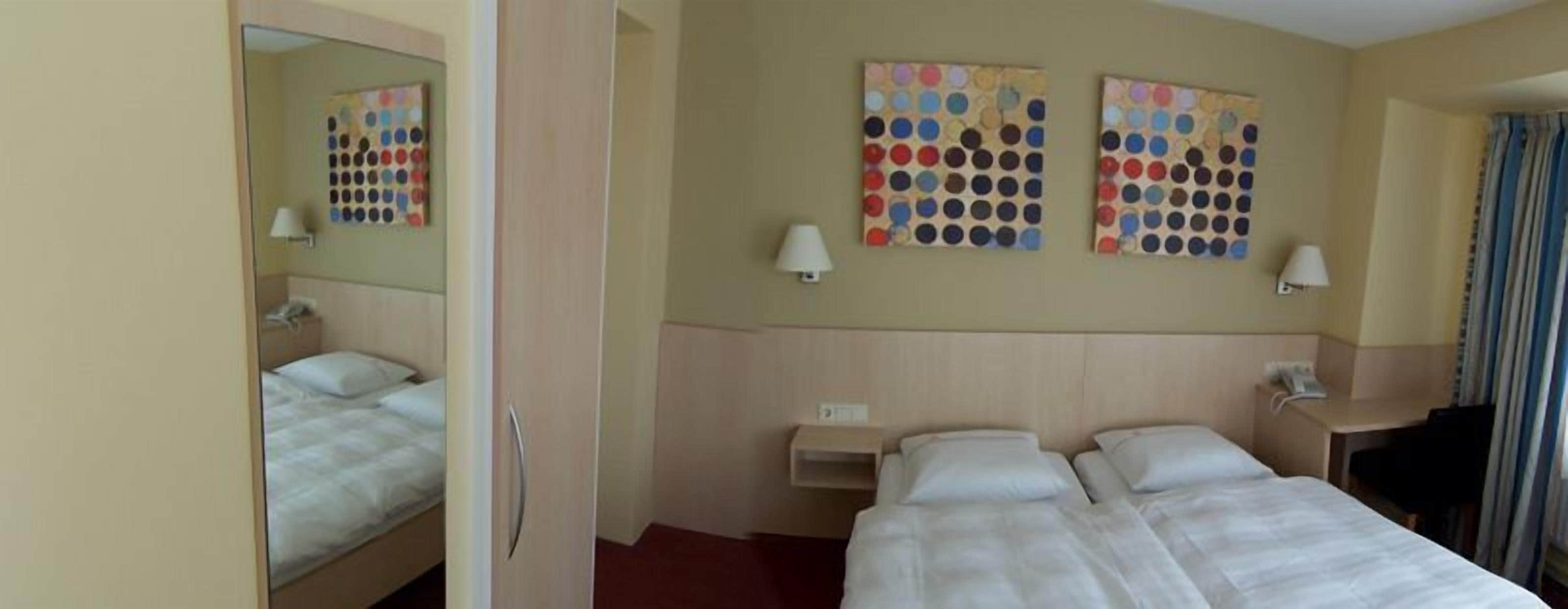 Habitación de hotel con cama, mesita de noche, espejo y dos obras de arte en la pared.