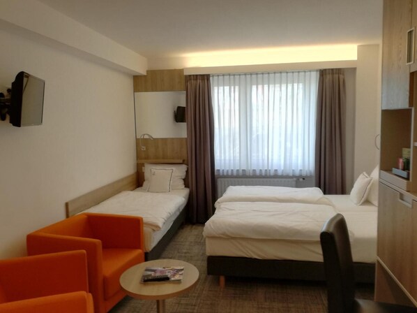 A hotel room with two beds, a sofa, a small table, a TV, and a window with curtains.