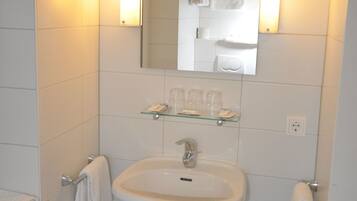 Un baño con lavamanos blanco, espejo y dos luces fijadas a la pared.