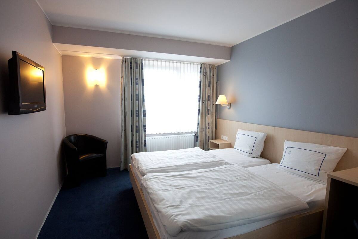 Une chambre d’hôtel avec un grand lit, une télévision, une chaise et une fenêtre avec des rideaux.