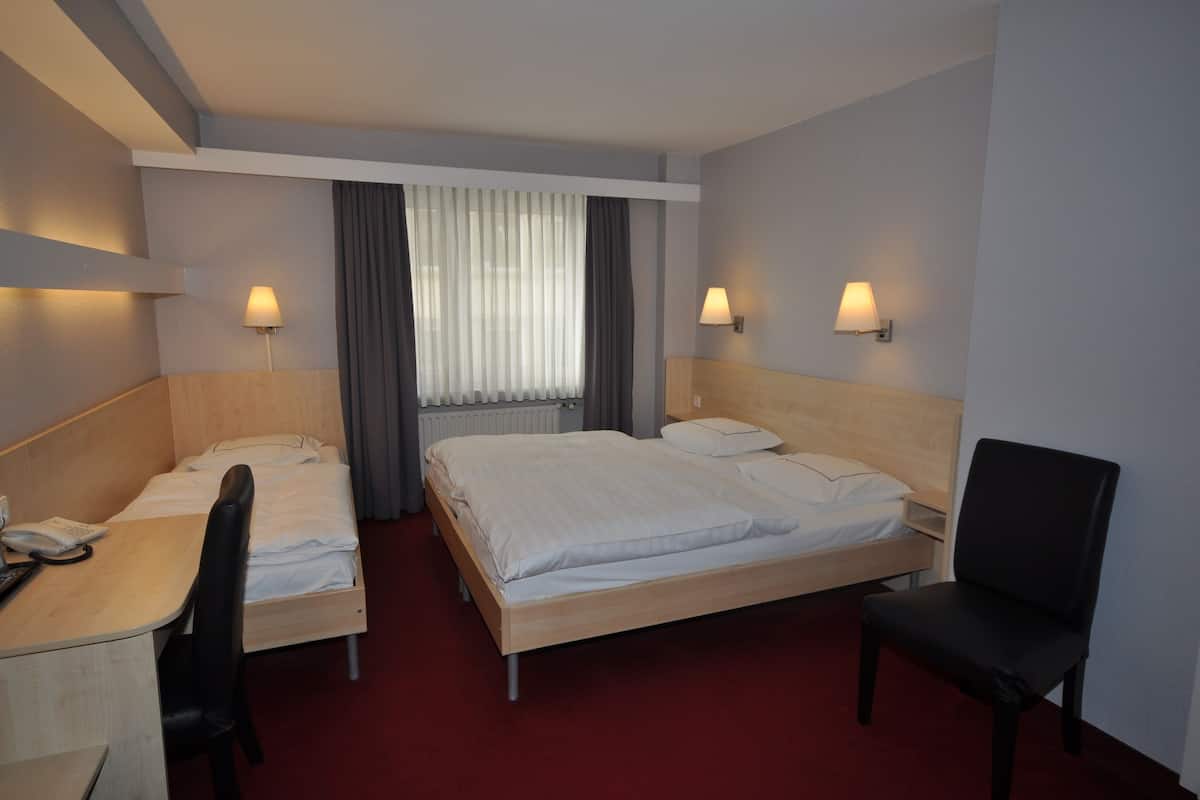 Une chambre d’hôtel avec deux lits, un bureau, une chaise et deux lampes fixées au mur.