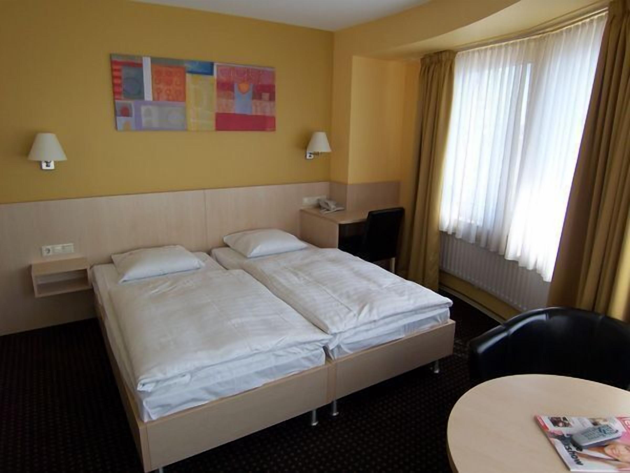 Ein Hotelzimmer mit zwei Betten, einem Schreibtisch, einem Stuhl und einem Fenster mit Vorhängen.