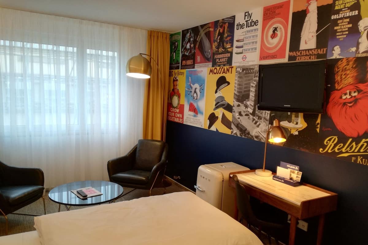 Une chambre d’hôtel équipée d’un lit, d’un bureau, d’une chaise, d’une lampe et d’un mur décoré d’affiches de films.