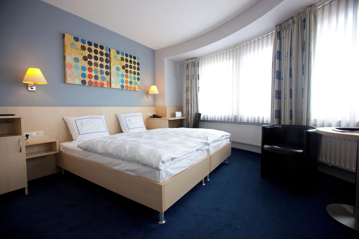 Une chambre d’hôtel avec un lit double, des tables de chevet, un bureau, une chaise et une grande fenêtre avec des rideaux.